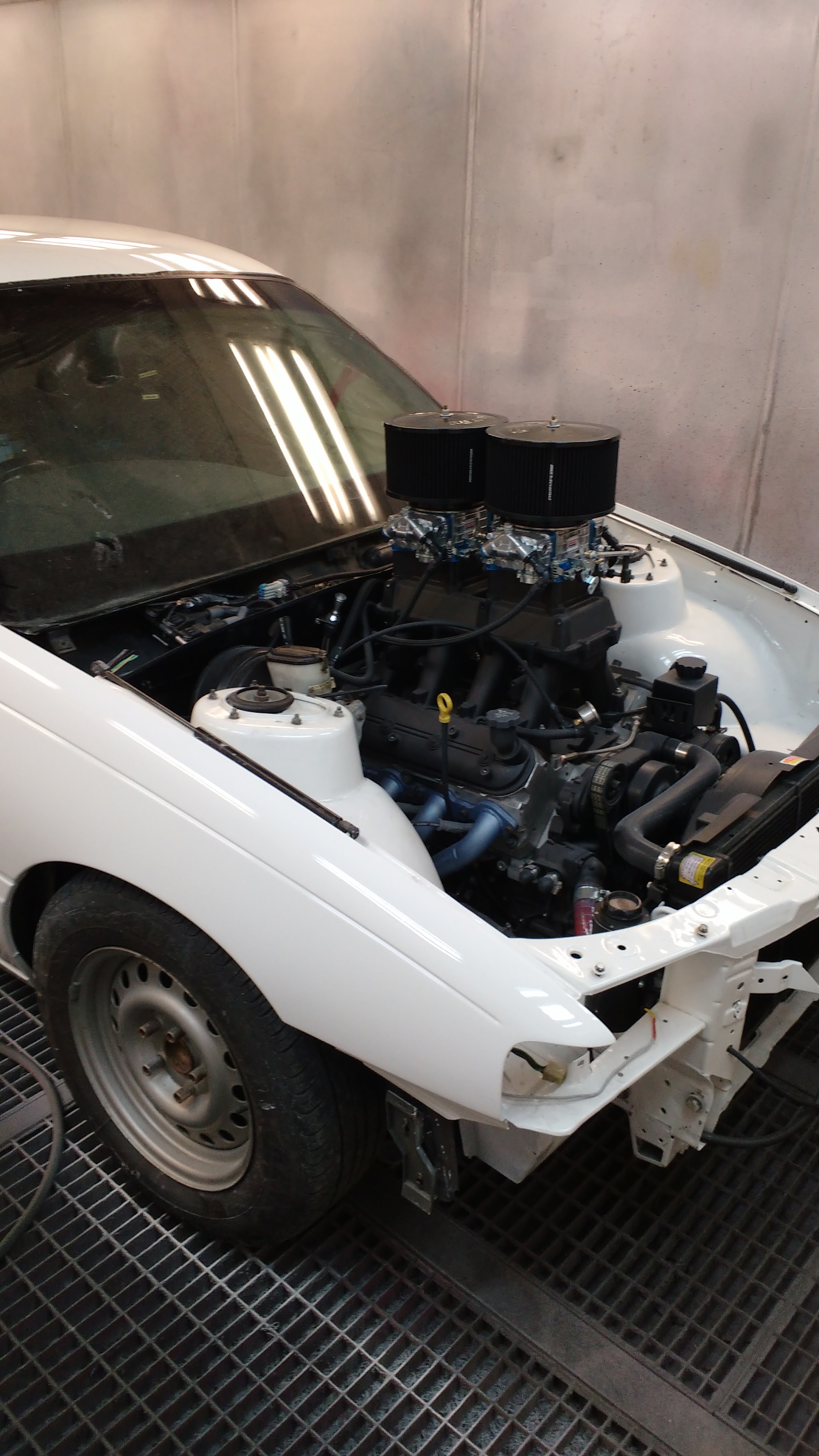A white classic Ford with a twin-carb V8 engine swap in the workshop